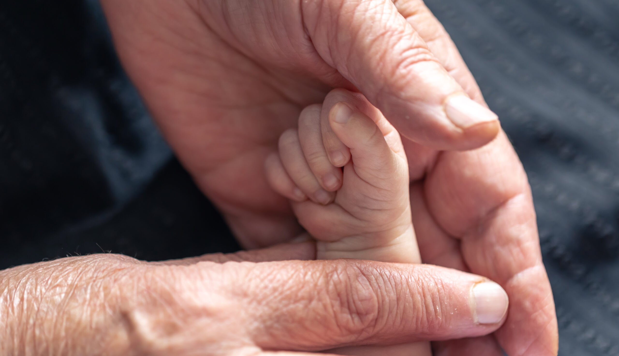 Close-up of an elderly hand gently holding a baby's tiny hand, symbolizing the emotional impact of premature aging.