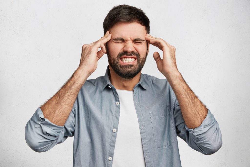 A bearded man closes his eyes and holds his head in pain, symbolizing ways to manage headaches without paracetamol.