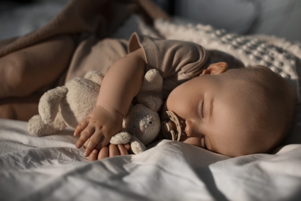 A cute baby peacefully sleeping with a pacifier and soft toys, highlighting the challenge of ensuring restful sleep.