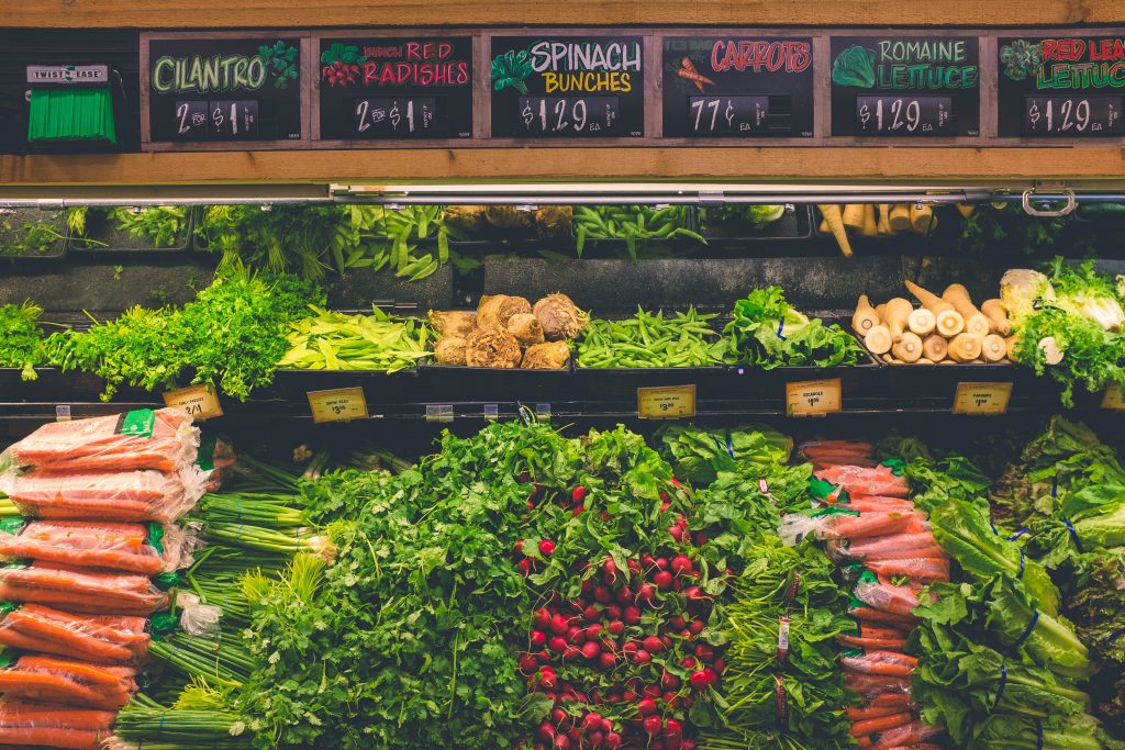 Cilantro, red radishes, spinach bunches, carrots, and other fresh vegetables displayed on a supermarket rack.