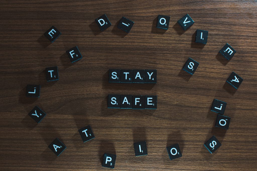 The words 'Stay Safe' spelled with Scrabble tiles on a wooden table, emphasizing protection from COVID-19 and infections.