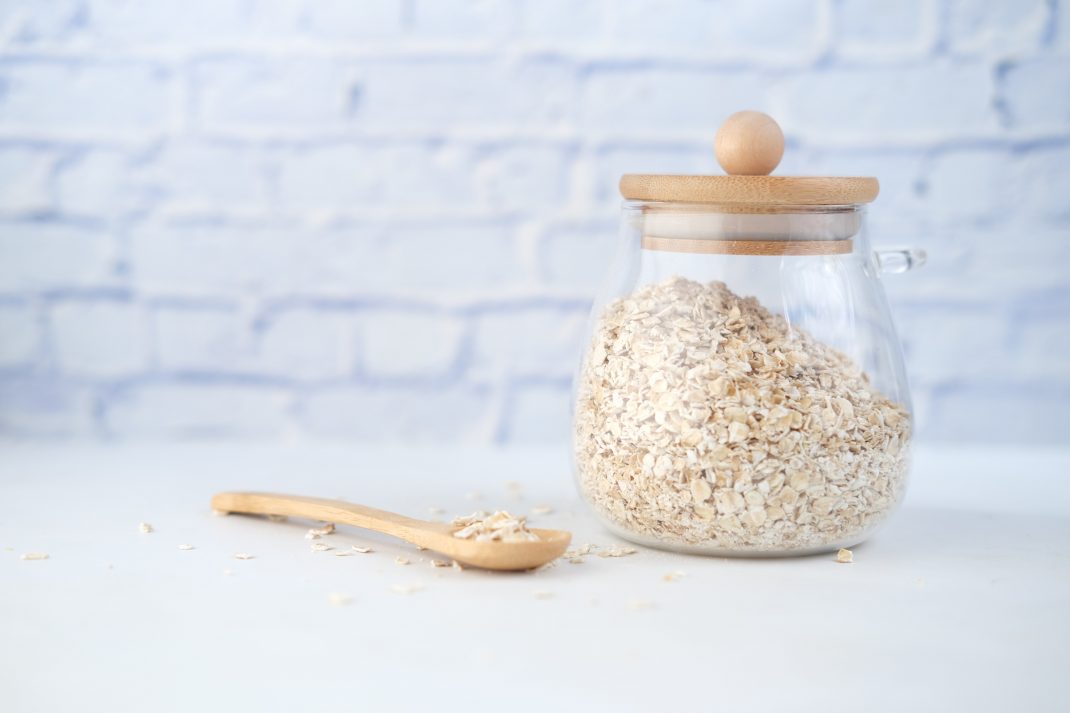 A glass jar of oats with a wooden lid and spoon, showcasing the health benefits of oats being incredibly good.