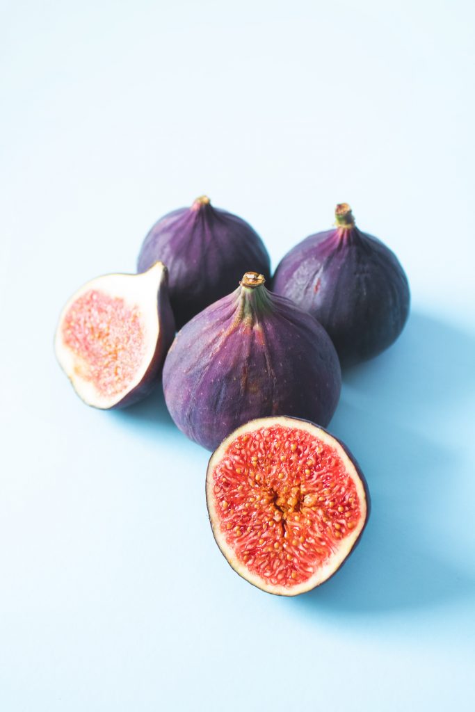 Figs neatly arranged against a light blue backdrop, with one fig sliced in half, showcasing their rich source of calcium, potassium, and fiber.