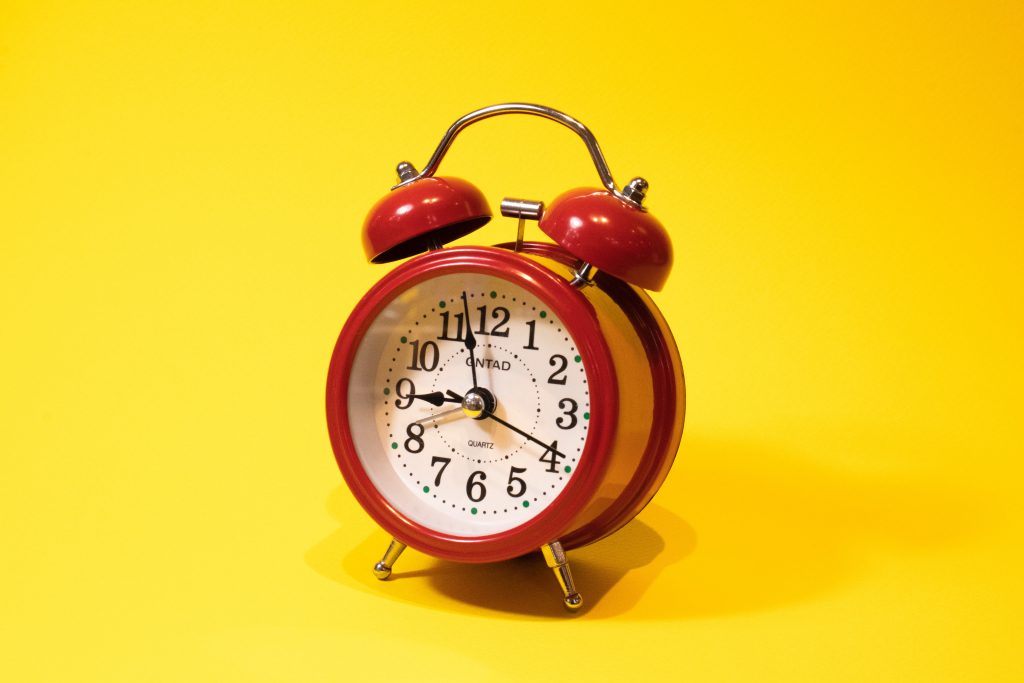 An elegant picture of a red alarm clock against a yellow background.