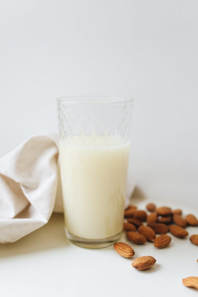 A glass filled with almond milk surrounded by scattered almonds on a white background.
