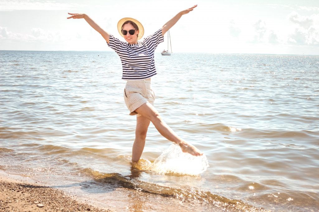 A woman happily posing on a beach on a bright sunny day, radiating joy and relaxation.