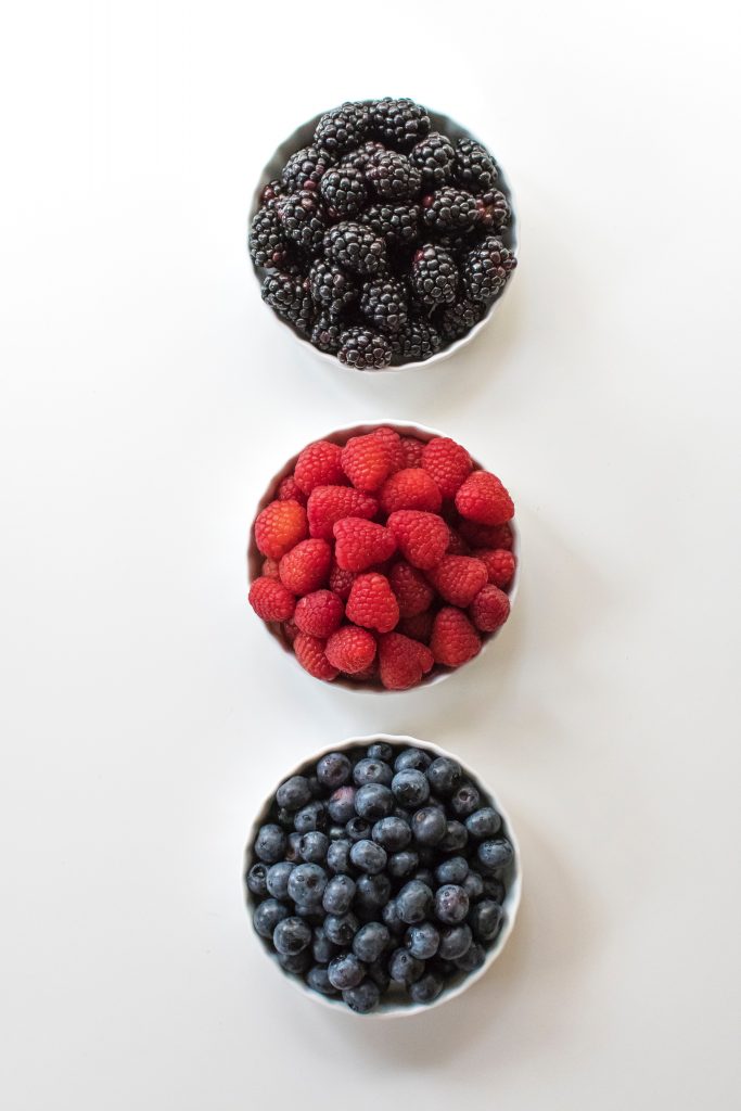 Strawberries, blackberries, and raspberries, each rich in fiber and water, neatly arranged in white bowls.