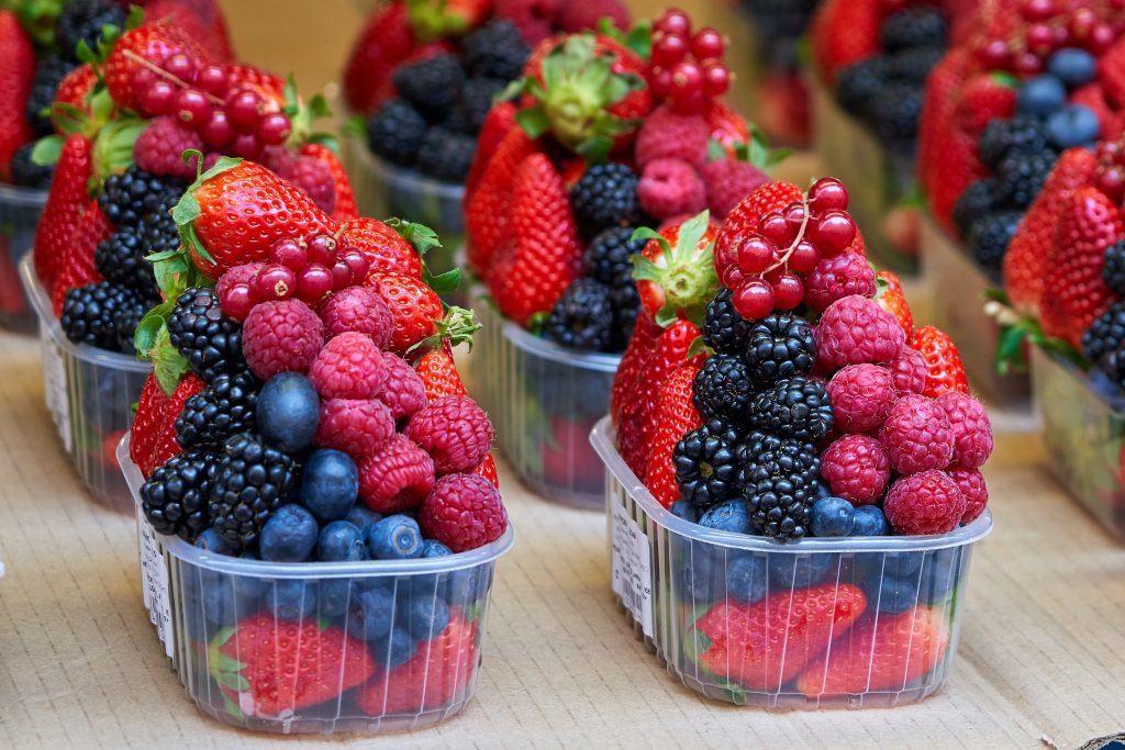 A row of plastic bowls filled with mixed berries, supporting artery flexibility and heart health for lower blood pressure.