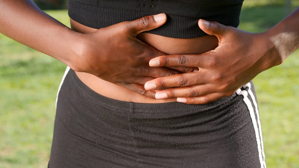 A close-up shot of a woman holding her stomach, appearing to struggle due to bloating.
