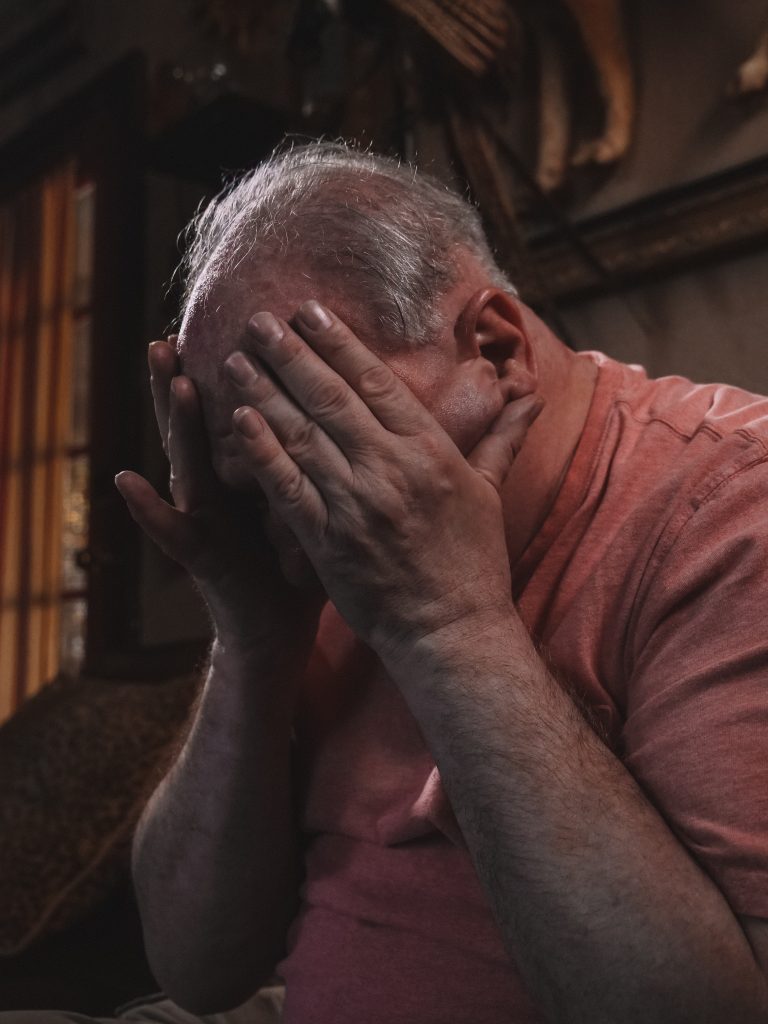 An elderly man holding his head, visibly suffering from brain fog.