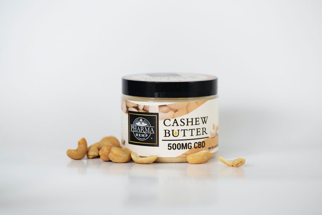 A jar of creamy cashew butter displayed on a white surface, with a handful of cashews lying scattered nearby.