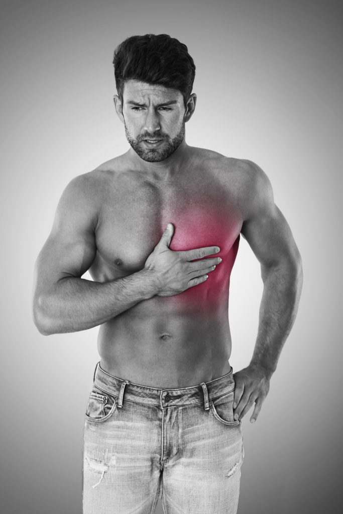 A young man in distress, holding his chest in pain, depicting a moment of chest discomfort or potential heart issues.