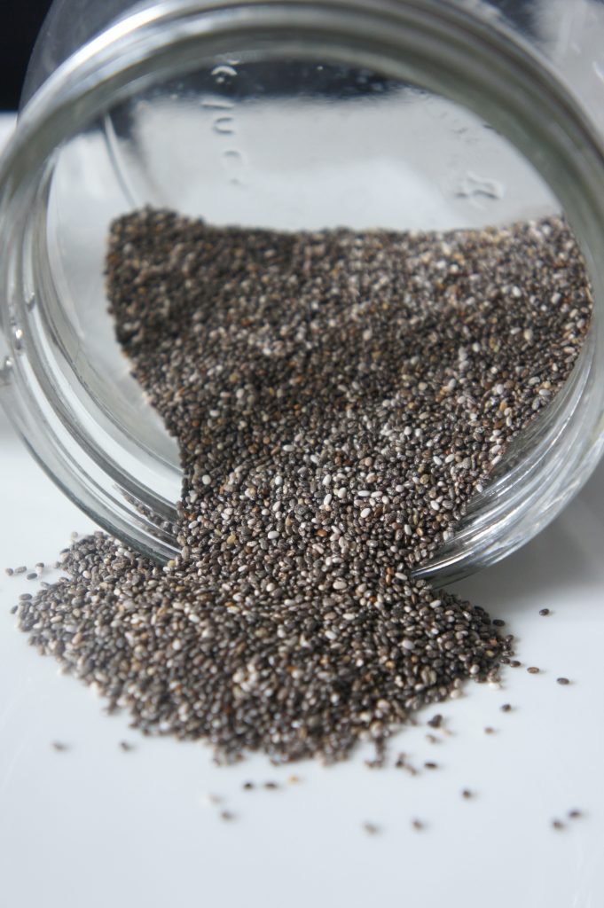 Close-up shot of chia seeds, beneficial for blood sugar control, spilled from a glass jar onto a white surface