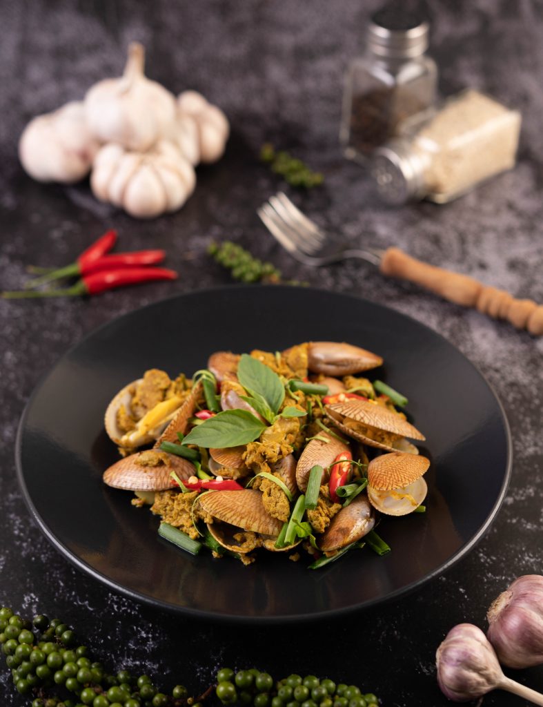 Curry powder stir fry on a black plate along with garlic, chilly and basil.