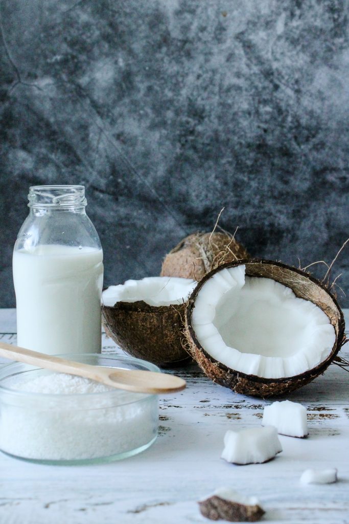 A bottle of coconut milk alongside a whole coconut and coconut flakes.