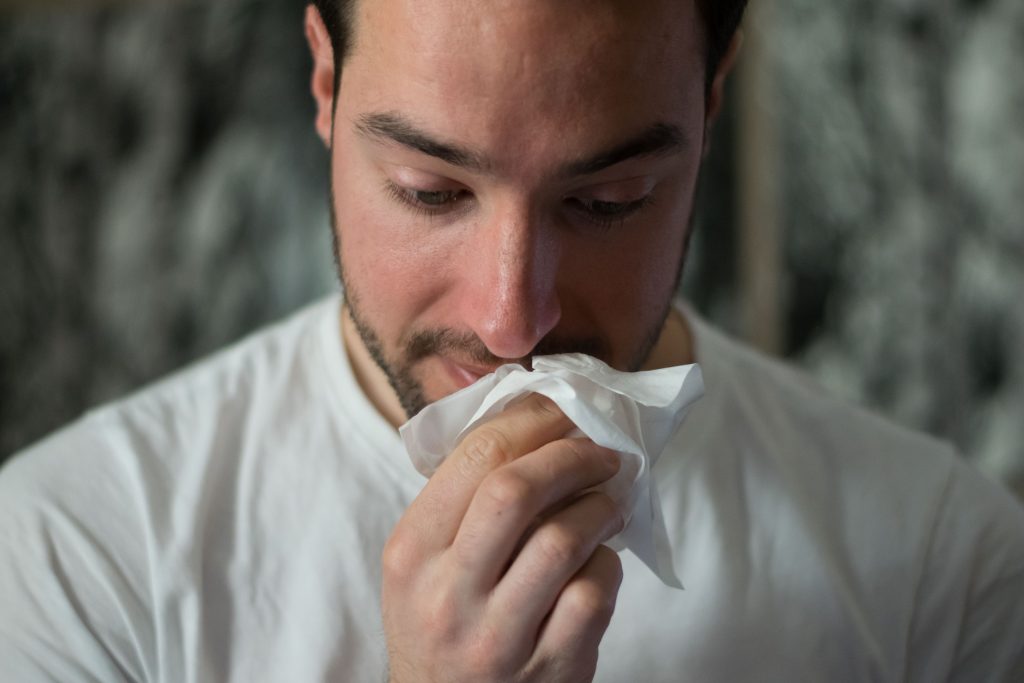 A man suffering from a cold, wiping his nose with a tissue.