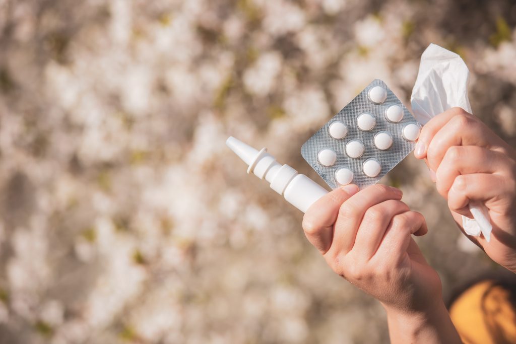 A close-up shot of a person's hand holding cold medicine, an inhaler, and a tissue.