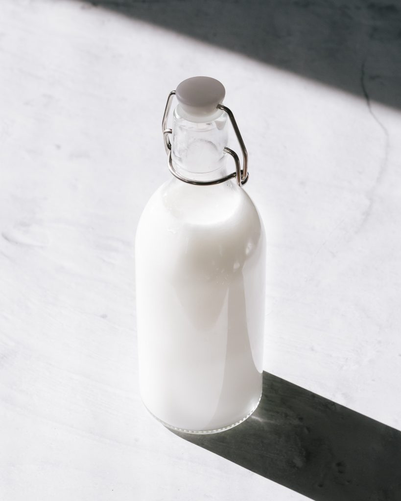 A glass bottle with a metal clasp and white cap containing soy milk.