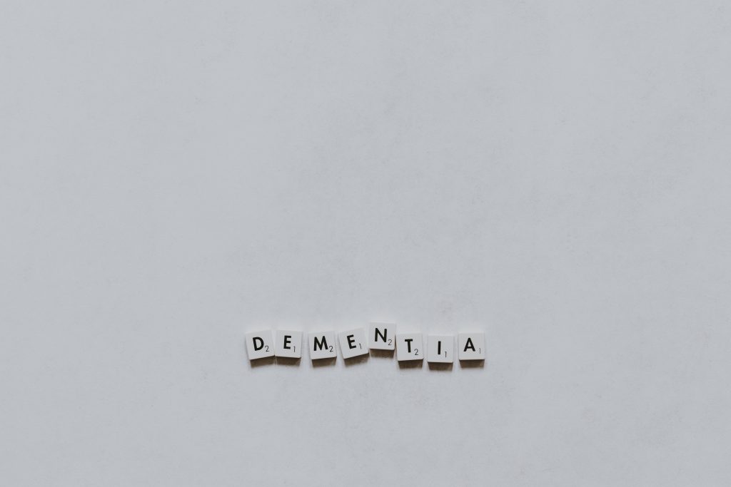 A long shot of white Scrabble tiles arranged to spell "DEMENTIA" on a white surface.