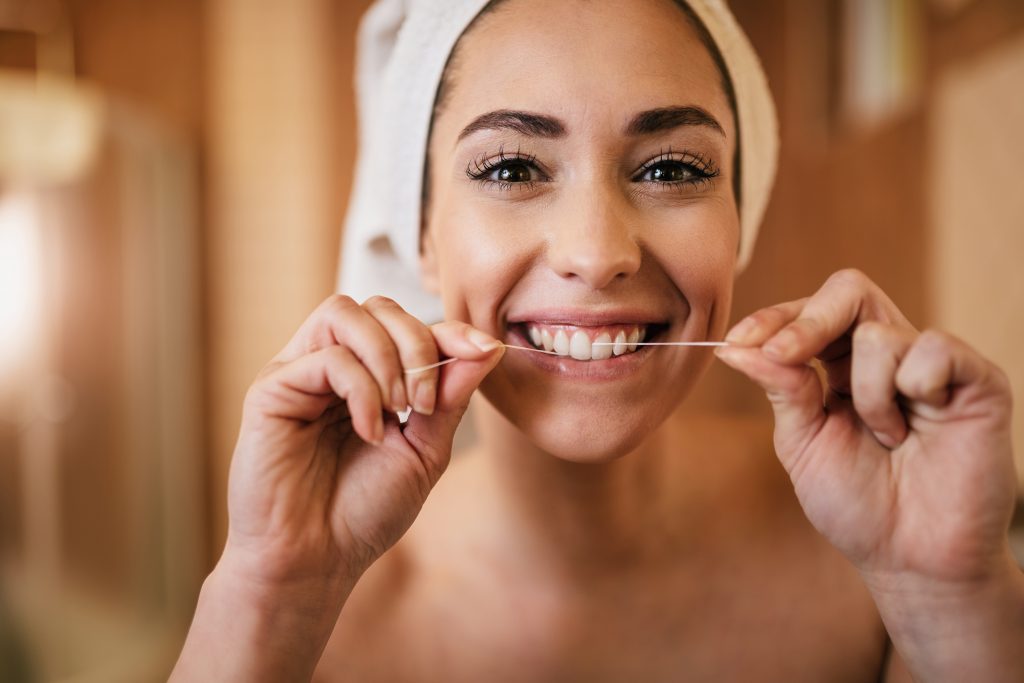 A happy, beautiful young woman flossing her teeth with a bright smile.