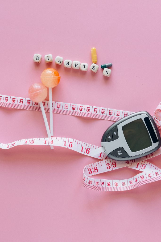 A blood sugar monitor, measuring tape, candies, pills, and alphabet blocks spelling "Diabetes" arranged together, symbolizing the importance of regular monitoring in controlling diabetes.