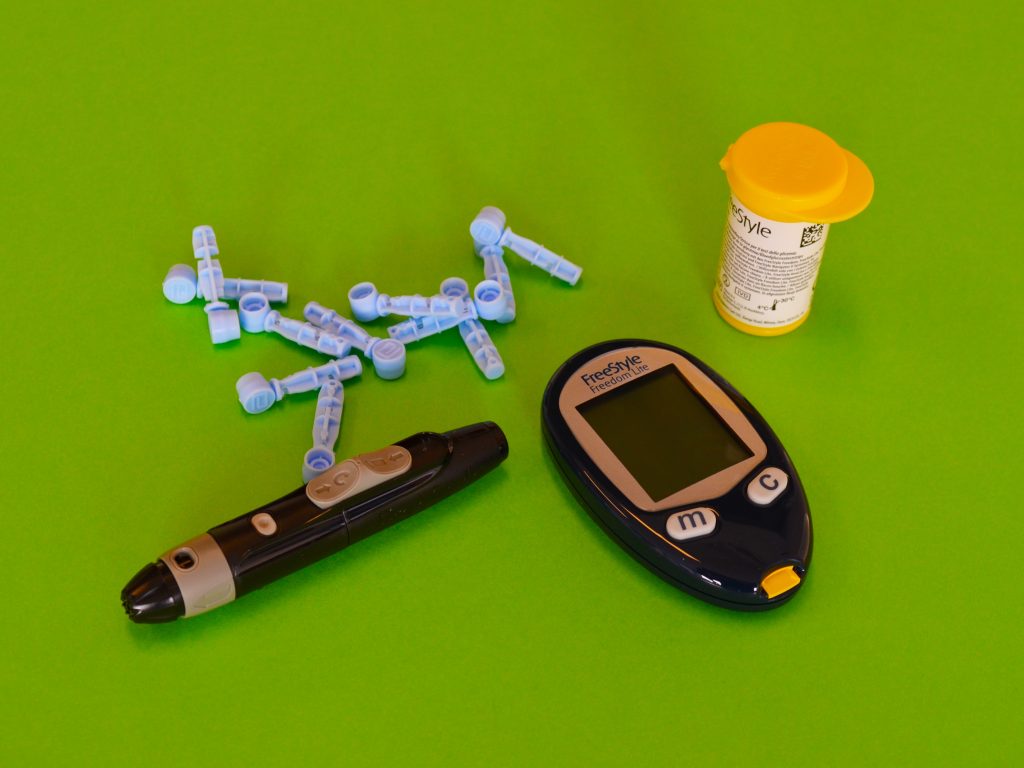 An aesthetic shot of a blood glucose monitor, test strips, and an insulin pen.