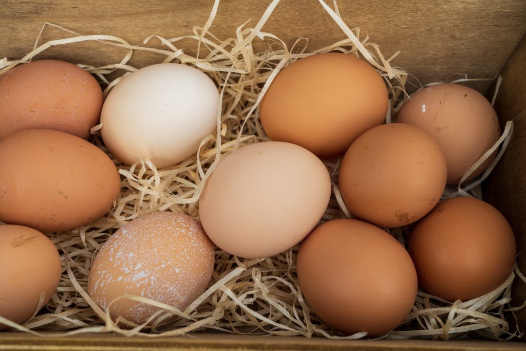 An aesthetic shot of brown and white eggs neatly arranged in a cardboard carton, resting on a bed of dried grass.