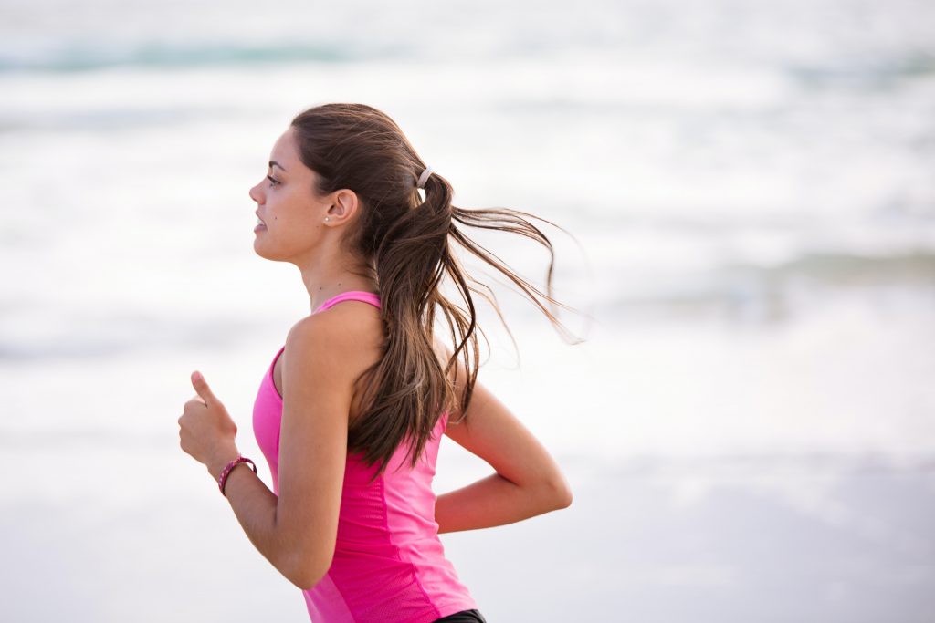 A young woman running along the sea shore, demonstrating the benefits of exercising at the right time for energy and health.