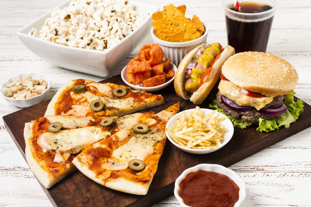 A variety of junk food dishes, including pizzas, burgers, French fries, and popcorn, neatly arranged on a table.