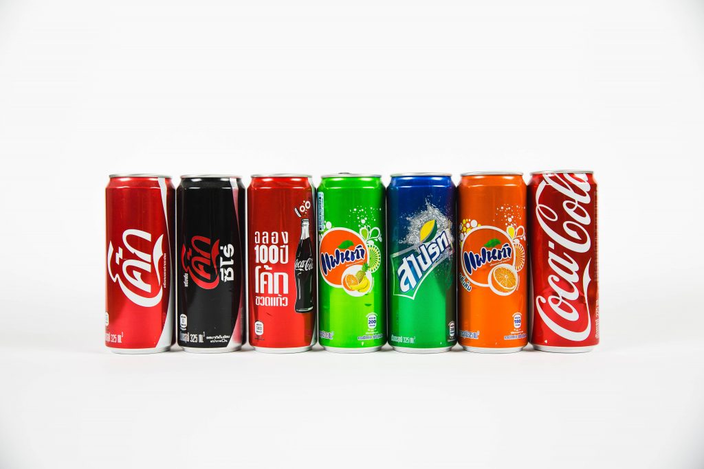 Different brands of fizzy drink cans arranged horizontally.