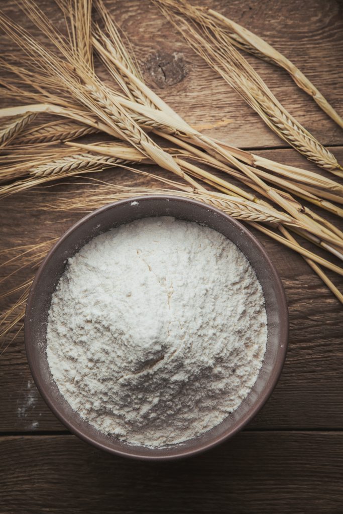 Wheat flour and freshly harvested wheat arranged on a wooden background.