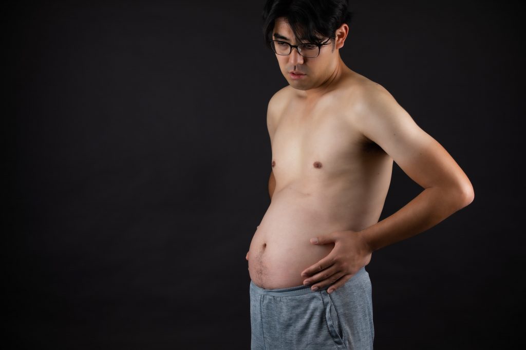 A man holding onto his bloated stomach, visibly uncomfortable.