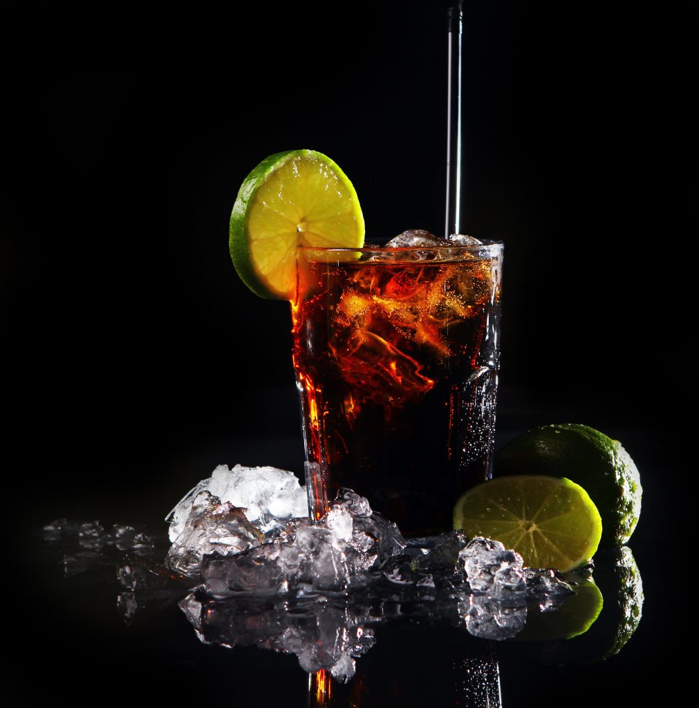 Fresh cola drink with ice and green lime on black background