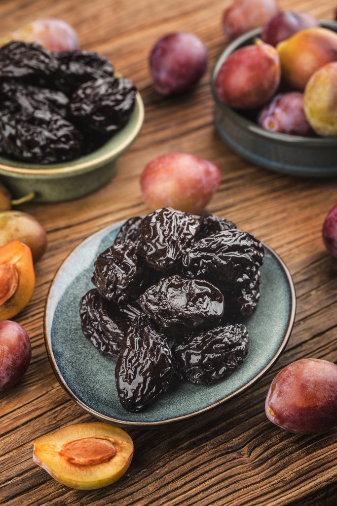 Dried prunes, rich in fiber, aesthetically presented on a plate with a few fresh prunes nearby.