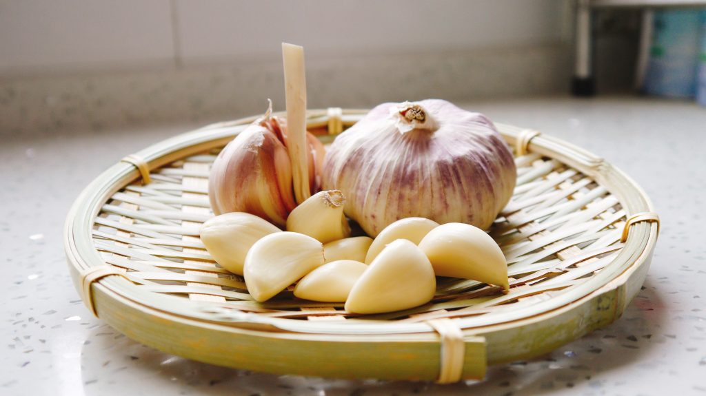 Two pods of garlic along with a few garlic cloves arranged on a woven bamboo plate.