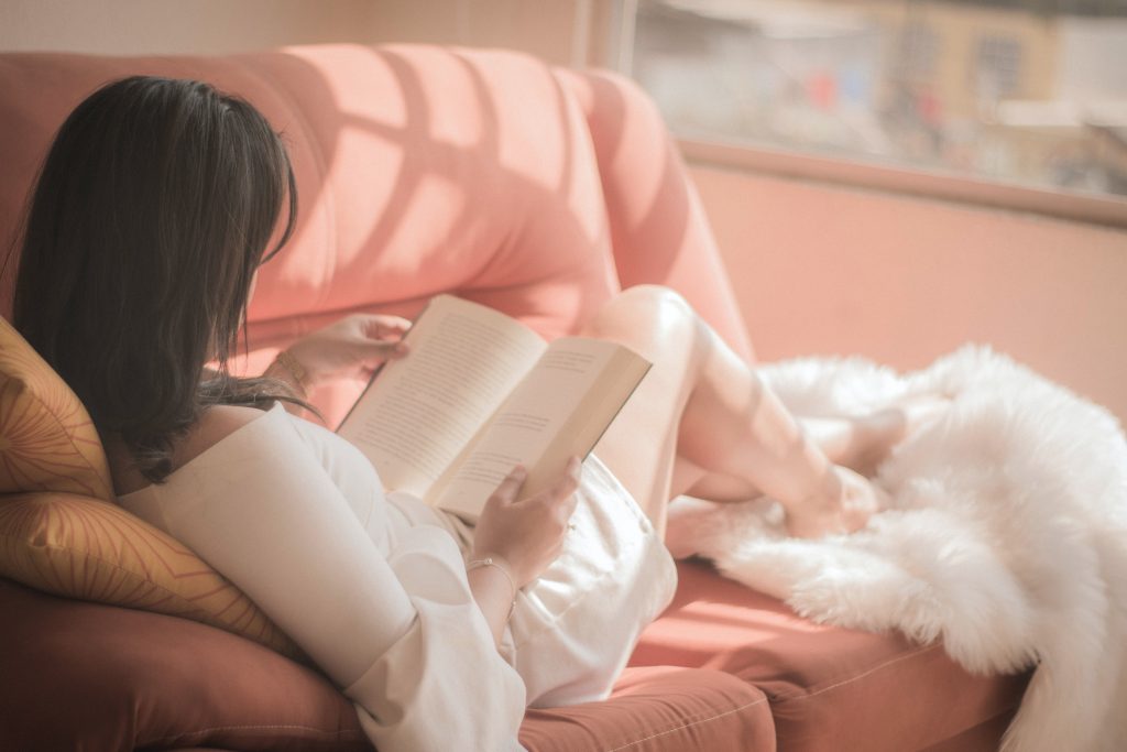 A woman peacefully lying on her couch, reading a book.