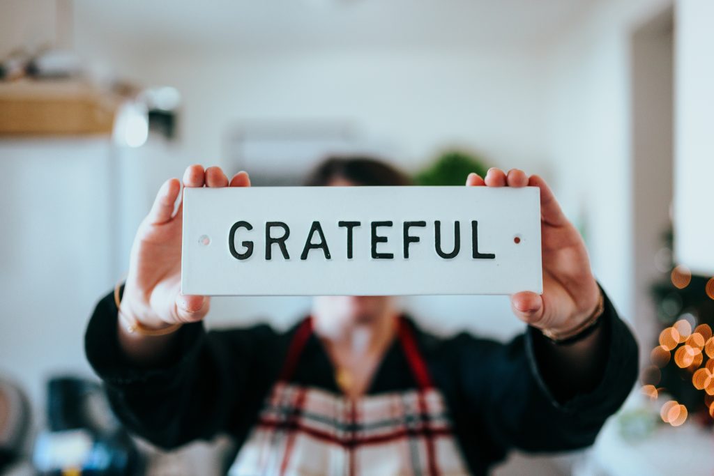 A woman holding and raising a name card with the word "GRATEFUL" written on it.