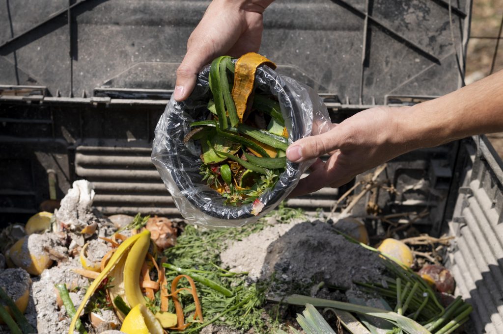 Food waste being discarded into an outdoor compost bin.
