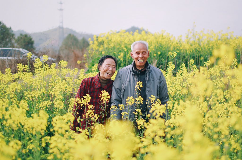 A couple happily smiling, amidst a mustard farm.