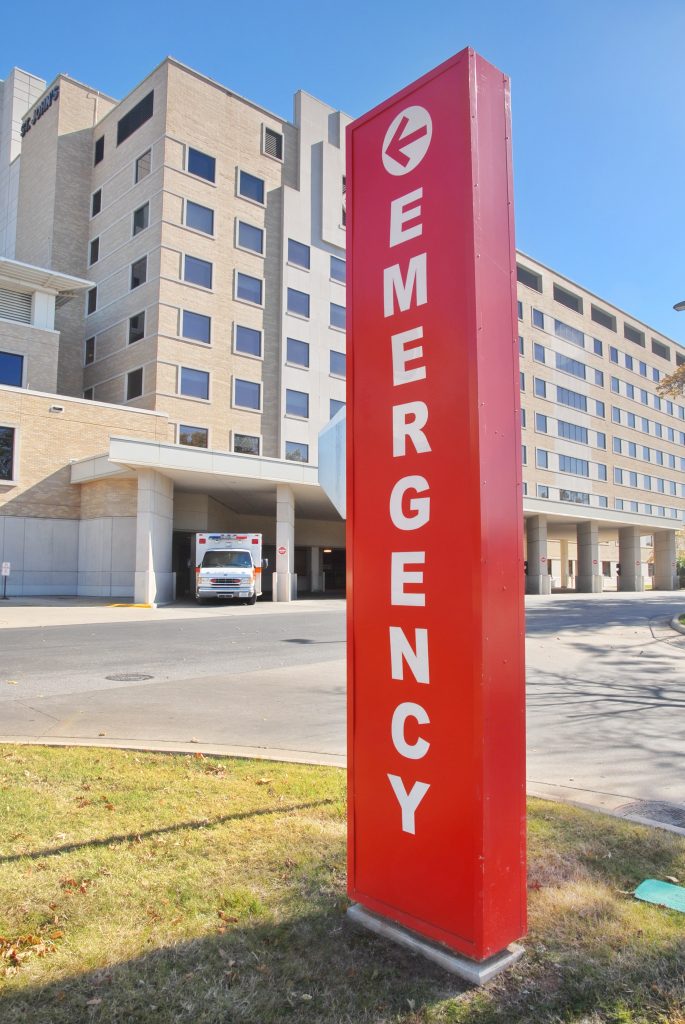 An "EMERGENCY" sign displayed in front of a hospital, indicating immediate medical attention is available.