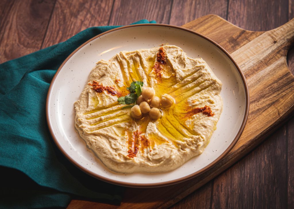 Hummus made with chickpeas, sesame seed paste, oil, and lemon, neatly presented on a white plate.