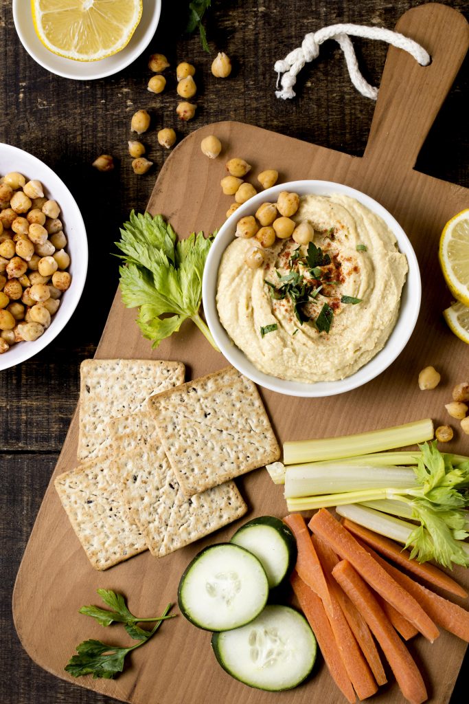 A beautiful shot of hummus with veggies, chickpeas, and dip arranged on a wooden platter.
