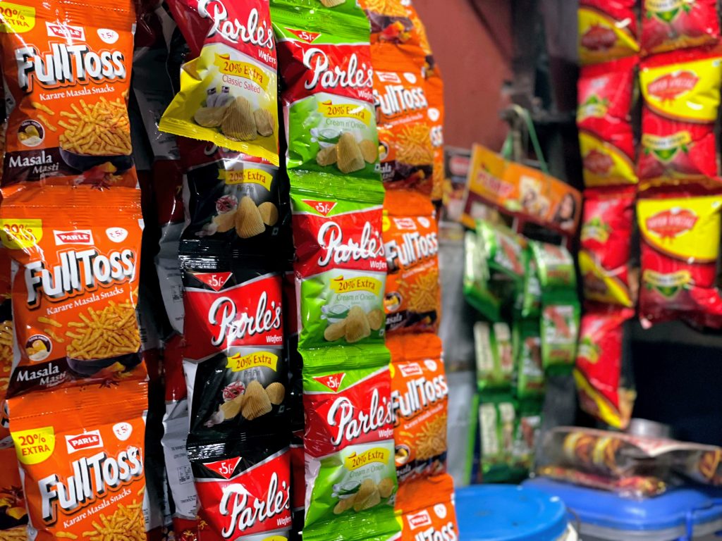 Sachets of junk food items like chips and fritters on display at a small shop.
