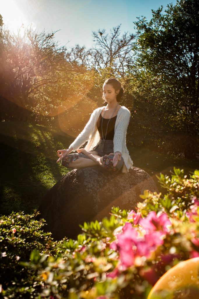 A young woman meditating peacefully in an open natural setting.