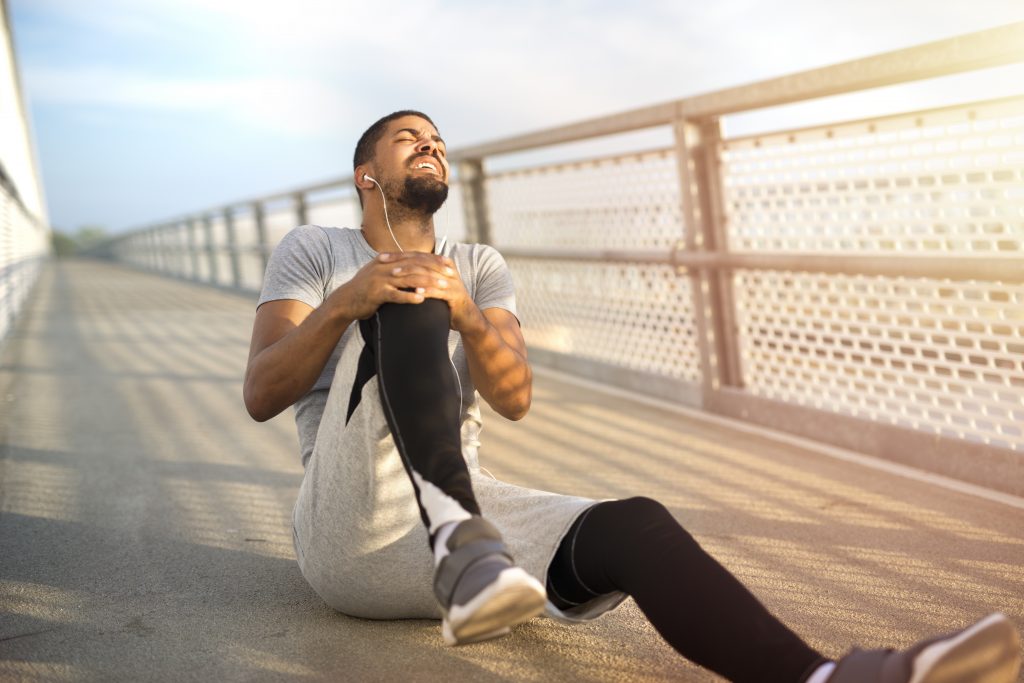 A man sitting on the ground holding his knee in pain, highlighting a possible symptom of magnesium deficiency.