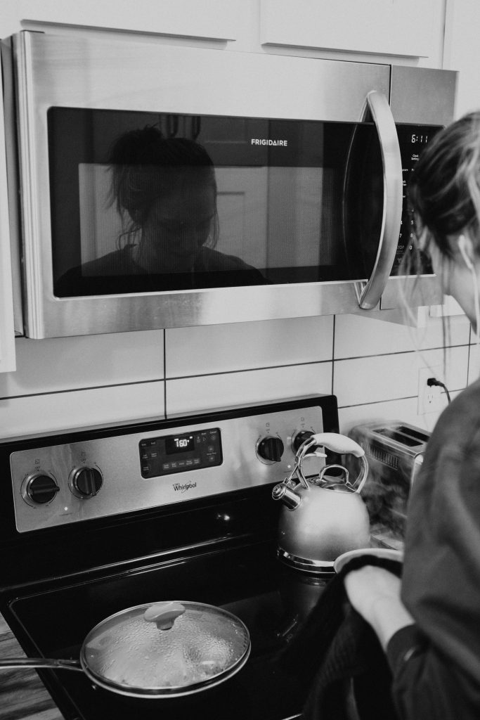 A woman cooking on a stove with a microwave in the background, illustrating the myth that microwave ovens do not cause cancer.