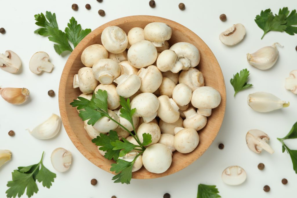 An appealing shot of button mushrooms with cilantro on top, presented in a bowl with a few spilled around.