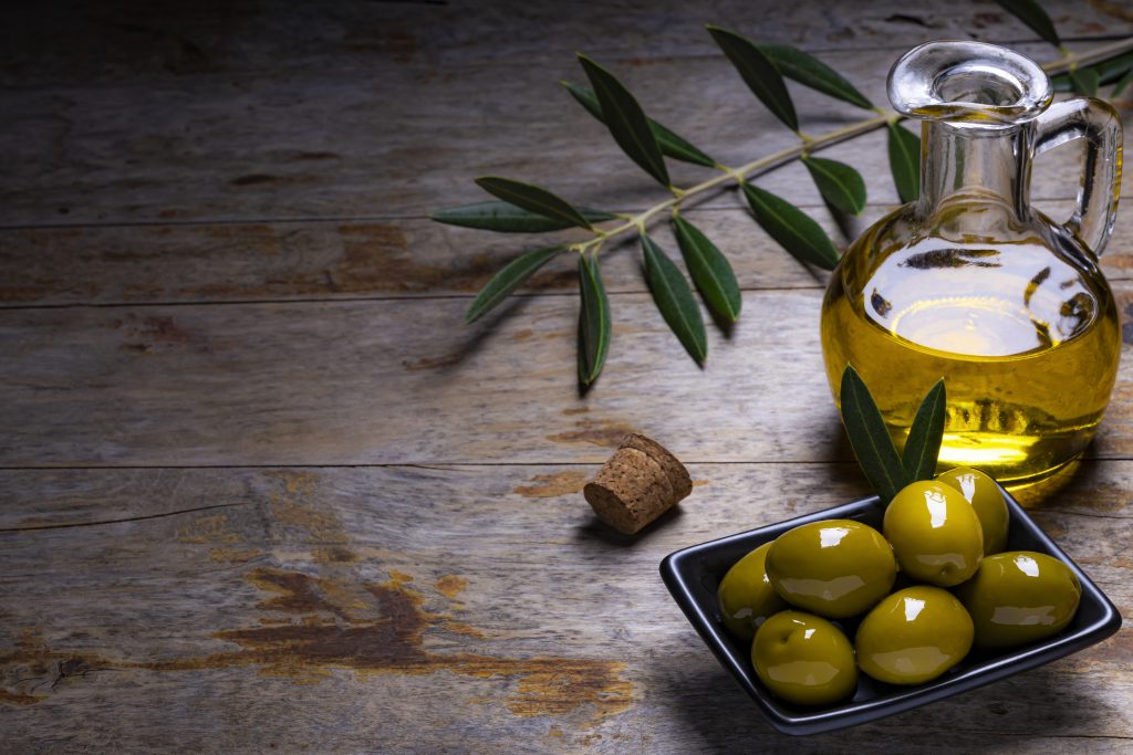 A jar of extra virgin olive oil displayed alongside a bowl of olives.
