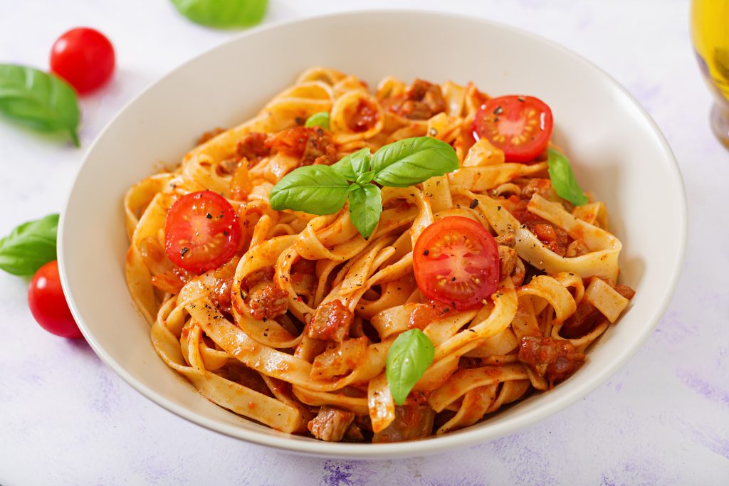 An appetizing shot of Pasta Fettuccine Bolognese with rich tomato sauce, beautifully served in a white bowl.