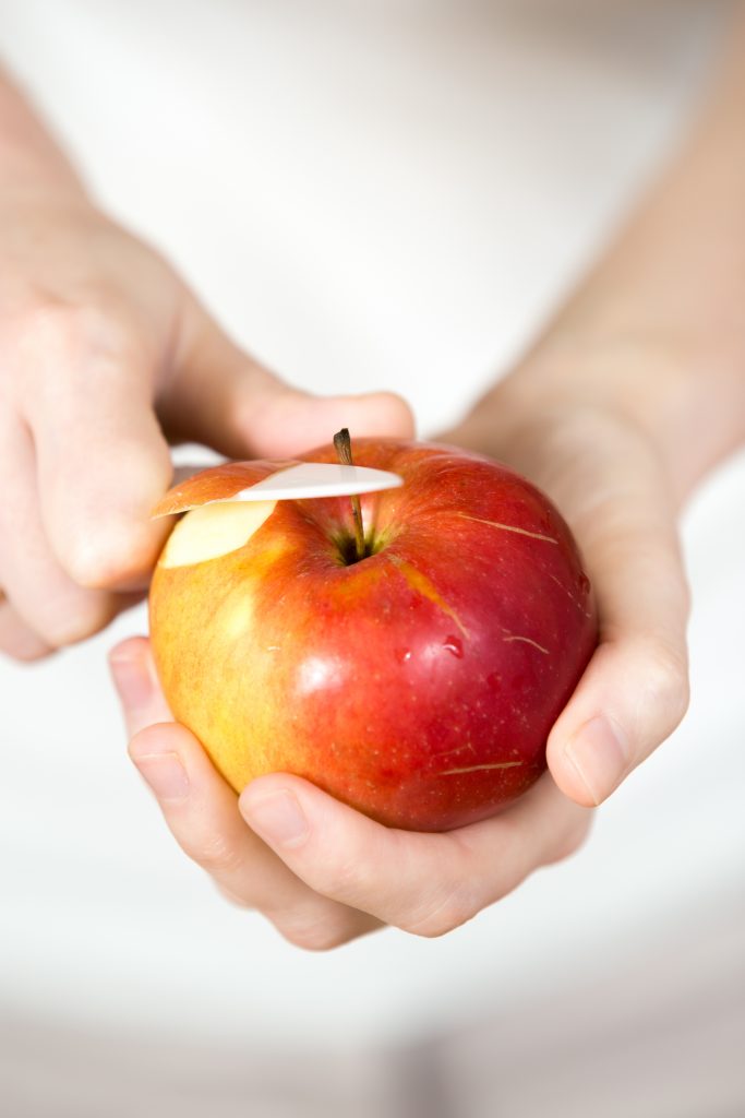 Close-up of a woman's hands neatly holding and peeling a red apple.